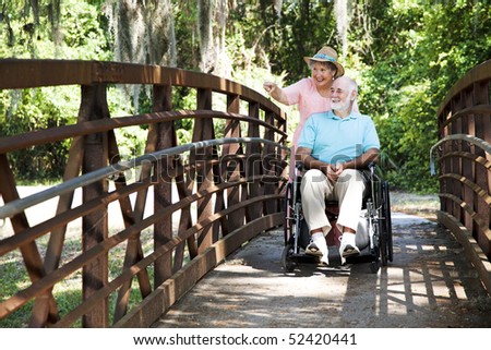 Senior woman pushing her disabled husband through the park in his wheelchair.
