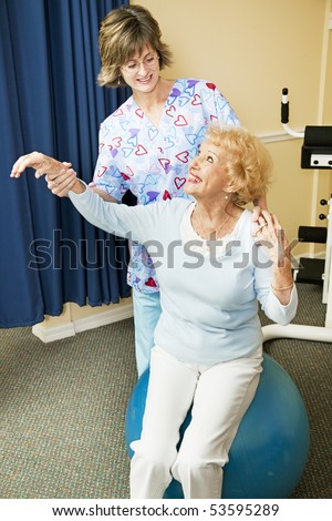 Physical therapist helps senior woman workout on a pilates ball.