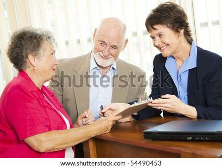 Senior couple working with a broker or adviser, signing paperwork.