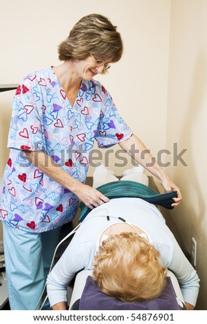 Physical therapist in chiropractors office, applying electrical stimulation therapy to patient.