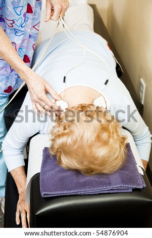 Physical therapist placing electrical stimulation pads on a patient\'s back to relieve muscle pain.