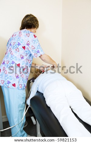 Physical therapist in chiropractic office applies electrical stimulation to a patient\'s back.