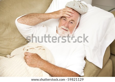Senior man home sick in bed, with an ice pack on his head.  Could be hangover or illness.