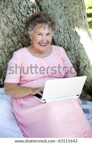 Senior woman outdoors under a tree, using her new netbook computer.