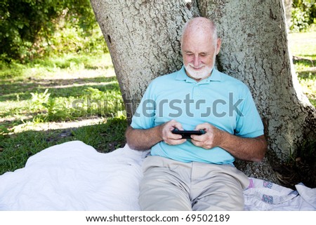 Senior man enjoys texting on his smart phone.  Wide view with room for text.