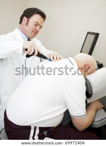Chiropractor using a modern, electronic tool to adjust and elderly patient\'s back.