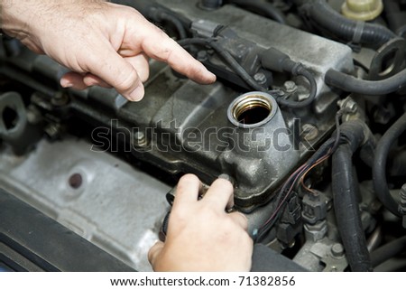 Father\'s hand pointing to the oil reservoir in the automobile engine.  Son\'s smaller hand holding the oil cap.