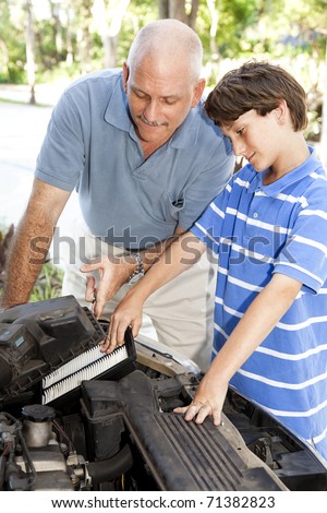 Boy helping his father change the air filter on the car engine.