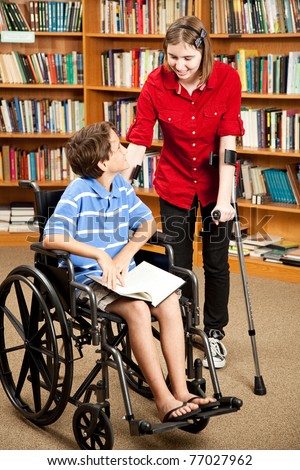 Disabled teen with forearm crutches, talking to a little boy in a wheelchair.  They are in the library.