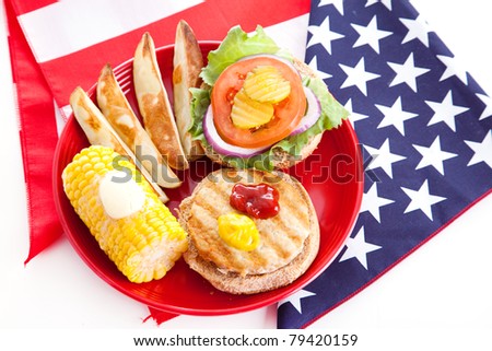 Healthy turkey burger on whole grain bun, with baked potato wedges and corn on the cob, for Fourth of July picnic.