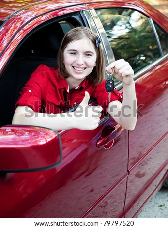 Teenage girl in the car driver\'s seat, holding keys and giving a thumbs up sign.