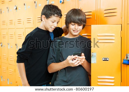Two teenage boys playing a handheld video game in school by their lockers.