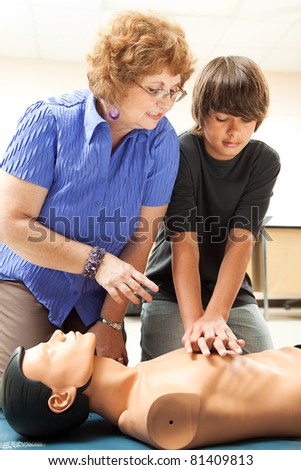 Teacher helping a teenage boy learn how to perform CPR.