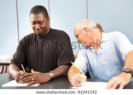 Older college student trying to copy off a younger student\'s test paper.