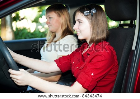Teenage girl driving her car with a friend in the passenger seat.