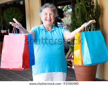 Happy senior woman holds up her arms full of shopping bags.