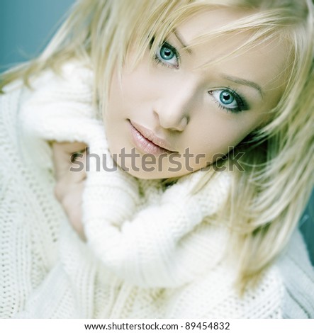 beautiful girl with perfect skin, blond hair and blue eyes in white sweater against a dark background