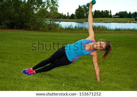 Woman doing side planks with dumbbells in a park.