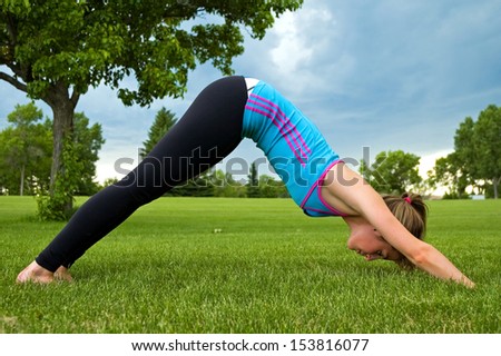 Young woman performing the Down Dog yoga pose, in a park.