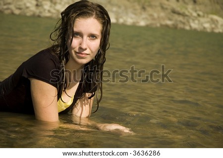 Cute soaking wet girl in a black dress, laying in the river.