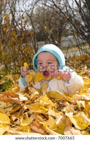 Baby girl sitting in a pile of leaves, and eating them.