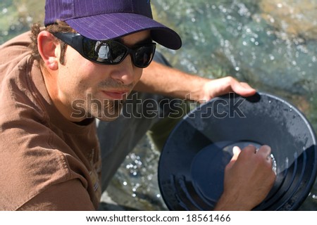 Rugged young man gold panning at a creek.