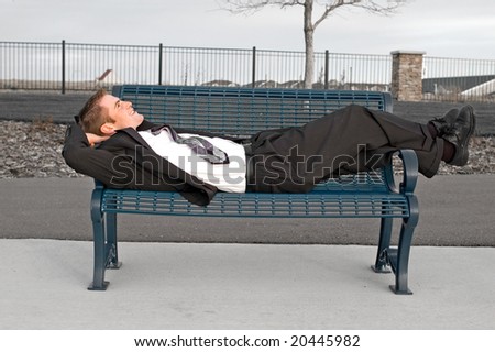 Happy young business man laying on a park bench.