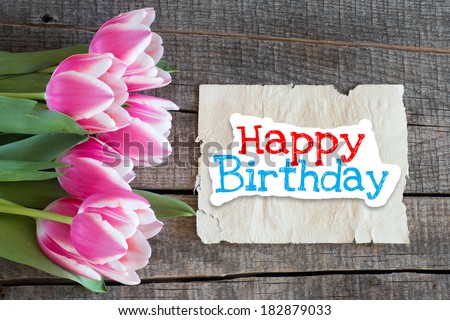 Happy birthday. Tulips and paper with text Happy birthday on wooden table