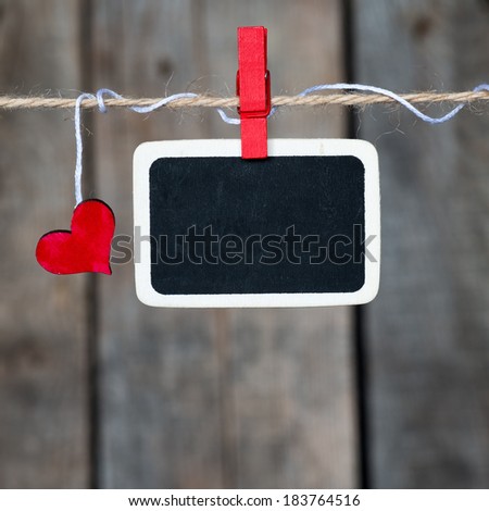 Blank small blackboard and small red heart hanging on the clothesline. On old wood background.