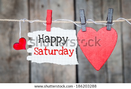 Happy Saturday on instant paper and small red hearts hanging on the clothesline. On old wood background