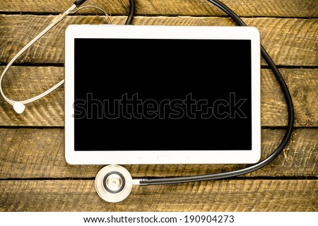 Medical stethoscope on modern digital tablet in laboratory on wood table. Concept of medical or research theme