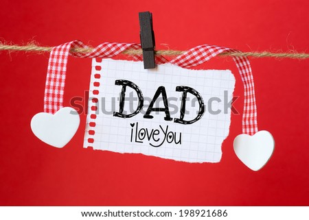 Dad I love you message written on a aged paper hanging on red background with two paper hearts