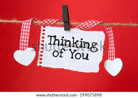 Thinking of You message written on a paper hanging on the clothesline on red background with two paper hearts