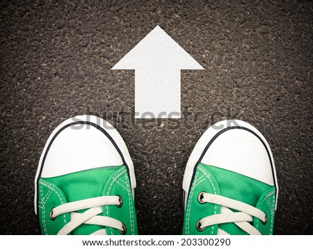 Male sneakers on the asphalt road with drawn direction arrow