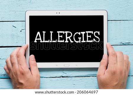 Hands hold tablet PC with text Allergies on wooden background