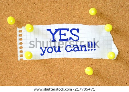 The phrase Yes You Can written by hand on a piece of paper pinned to a cork notice board