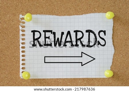 The word Rewards with an arrow pointing in the right direction on a paper note pinned to a cork notice board