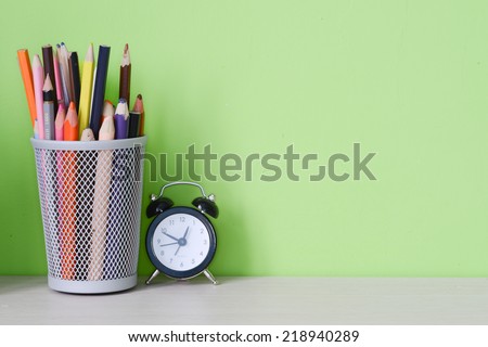 Pen box and clock on green wall background