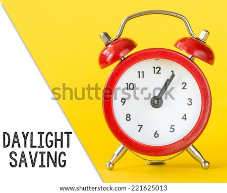Alarm clock on yellow background with text daylight saving.