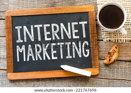 Internet marketing handwritten with white chalk on a blackboard, cup of coffee and biscuit on a wooden background