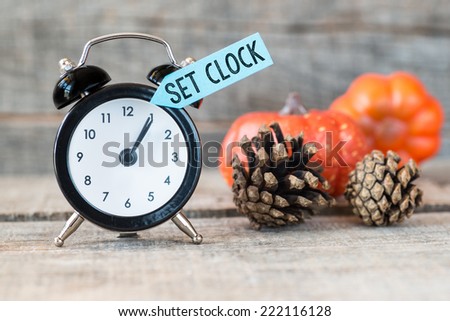 Black alarm clock with text set clock, pine cones and pumpkins on wooden background