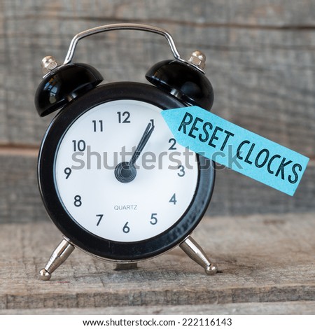 Black alarm clock with text reset clocks on wooden background