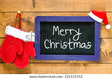 Merry Christmas. Christmas decorations with mittens and Christmas hat with place for greeting on chalk blackboard.