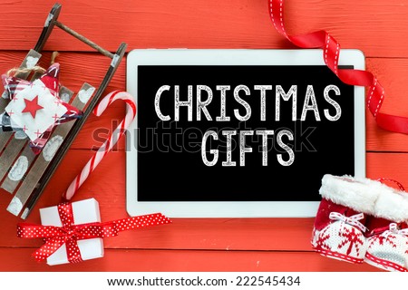 Christmas gifts inscription on white tablet on red wooden table. Sled and boots