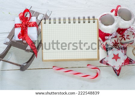 Notebook and Christmas decorations on wooden background. Sled, boots, candy, gift, star,