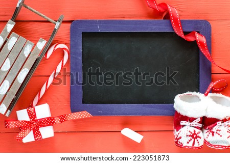 Christmas background. Blackboard with purple frame on red wooden table with christmas decorations : sled, boots, candy,and gift .