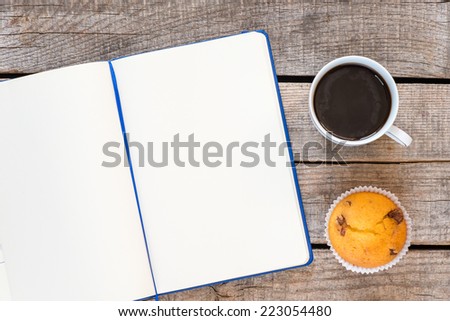 Open notebook, coffee and cupcake. Workspace with open notebook, coffee cup and muffin on old wooden table