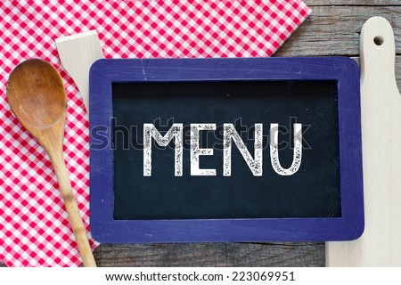 Chalked Menu on blackboard. Chalked word Menu on blackboard with wooden spoon and fork on a red checkered table cloth