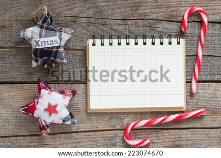 Christmas background. Checkered notebook on wooden table with Christmas textile stars and candies, background.