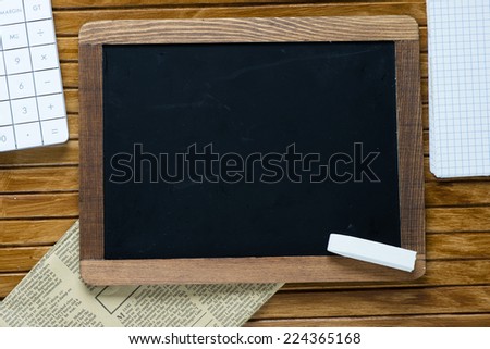 Small wooden framed blackboard with calculator, newspaper, notebook and chalk on wooden background